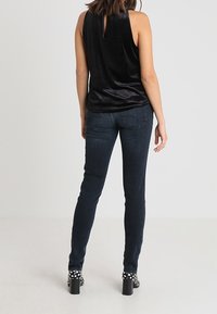 Ärmlös svart sammetstopp med nyckelhål på baksidan, parat med mörkblå slim-fit jeans och svarta klackar med vita prickar.