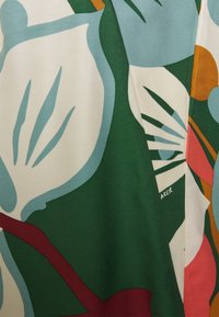 Tissu multicolore avec un motif floral présentant de grandes feuilles vertes, des accents bleu clair et des détails rouges et orange. Texture douce.