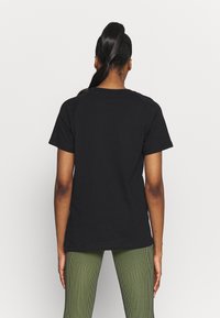 Camiseta negra de cuello redondo con mangas cortas, de corte relajado, hecha de un suave material de algodón. Presenta un diseño liso, vista desde la parte de atrás.