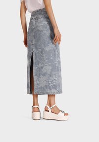 Gonna midi in denim azzurro chiaro con spacco laterale, caratterizzata da un motivo floreale testurizzato e tasche posteriori. Abbinata a sandali con zeppa.