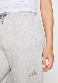 Sive trenirke iz mehkega blaga, z elastičnim pasom in vrvico ter majhnim logotipom na levi stegn. 