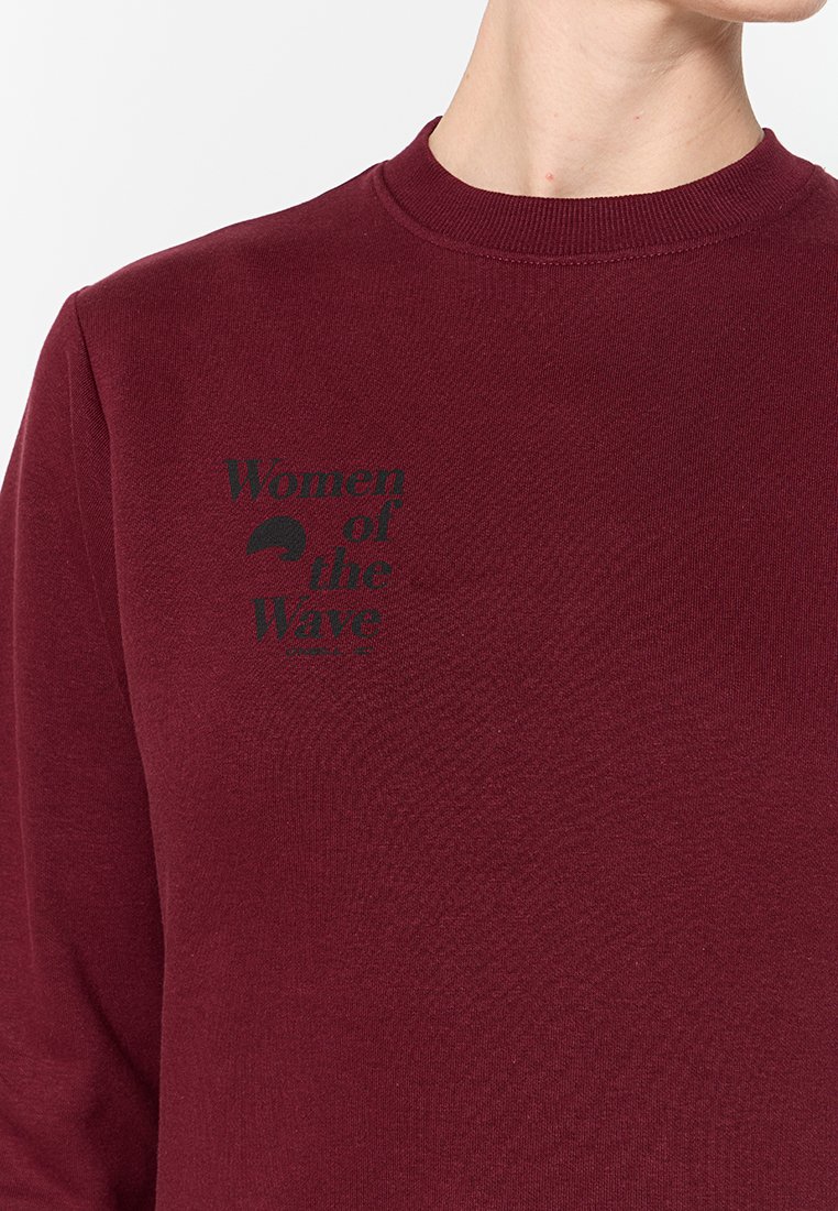 Sweat-shirt bordeaux avec un col rond et des poignets côtelés, portant la phrase « Femmes de la vague » imprimée en noir sur le devant.