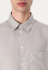 Überprüfte_button-up_hemden_in_beige_und_braun_mit_einem_Kragen,_einer_vorderen_Tasche_und_zwei_Sichtbaren_Knöpfen_am_Verschluss,_mit_einer_glatten_Oberfläche.