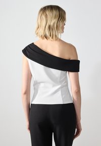 Asymmetrisk topp med svart drapert off-shoulder design og hvit tettsittende kropp. Glatt stoff og minimalistisk silhuett.