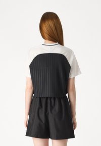 Kort t-shirt med vit fram- och svart baksida med smala ränder, korta ärmar och rund halsringning. Matchas med svarta shorts.