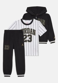 Crna zip-up dukserica i hlače s natpisom "23" i zlatnim Jumpman logotipima, upareni s bijelom majicom s kratkim rukavima i prugama "Jordan 23".