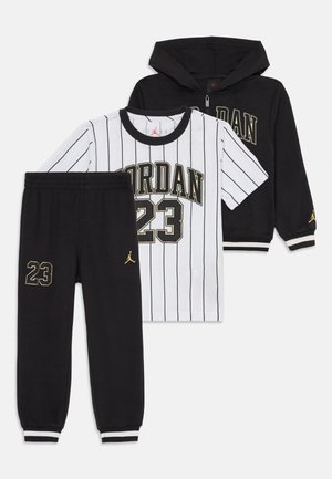Crna zip-up dukserica i hlače s natpisom "23" i zlatnim Jumpman logotipima, upareni s bijelom majicom s kratkim rukavima i prugama "Jordan 23".