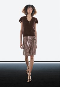 Brauner kurzärmeliger Strickpullover mit V-Ausschnitt, kombiniert mit einem roségoldenen Paillettenrock und schwarzen Sandalen mit Absatz, vor neutralem Hintergrund präsentiert.