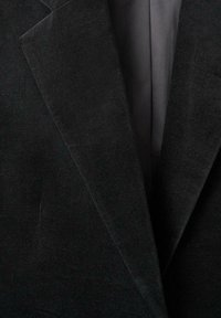 Gros plan sur les revers d'un blazer en velours noir montrant une texture douce et une doublure intérieure lisse.