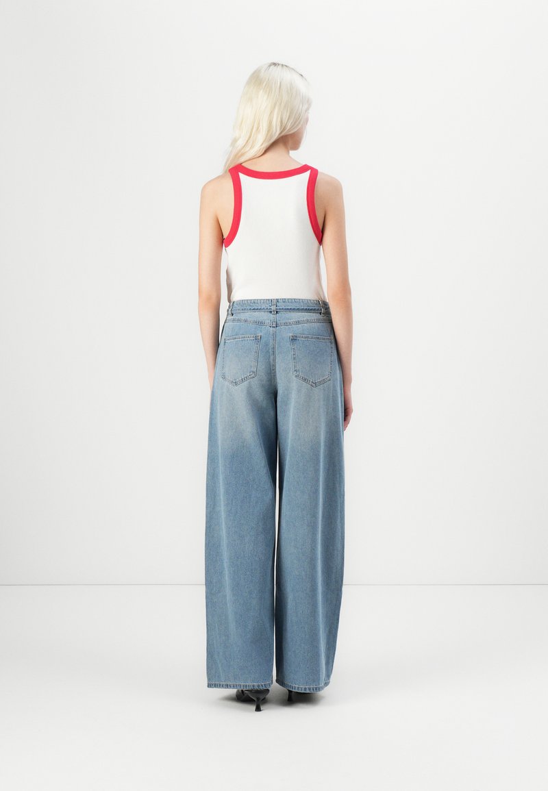 Witte tanktop met rode rand, gecombineerd met lichtblauwe denim jeans met hoge taille en wijde pijpen, voorzien van achterzakken en een relaxte pasvorm.