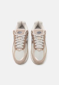 Baskets légères en daim beige et mesh. Bout arrondi, lacets blancs, et logo "N" argenté sur le côté.