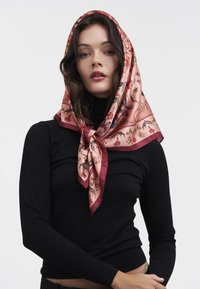 Silk firkantet tørklæde med et blomsterdesign i pink og røde nuancer, med en kontrasterende bordo kant, bundet pænt omkring modellens hoved.
