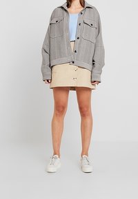 Chemise-robe à carreaux gris oversize, débardeur bleu clair, jupe à boutons beige, baskets blanches. Tenue décontractée en couches, coupe moderne.