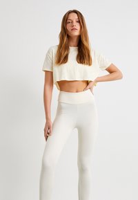 Afskåret lysegul tekstureret t-shirt parret med højderet, tætsiddende hvide leggings. Simpelt design med rene linjer og blødt stof.