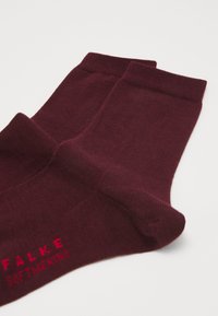 Burgunderfarbene Socken aus weichem Material mit glatter Textur. Mit gerippten Bündchen und rot gesticktem "FALKE SOFTMERINO"-Markenzeichen.