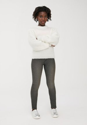 Maglione bianco e soffice a maglia con scollo tondo e maniche a sbuffo, abbinato a jeans slim-fit grigio scuro e sneaker argentate.