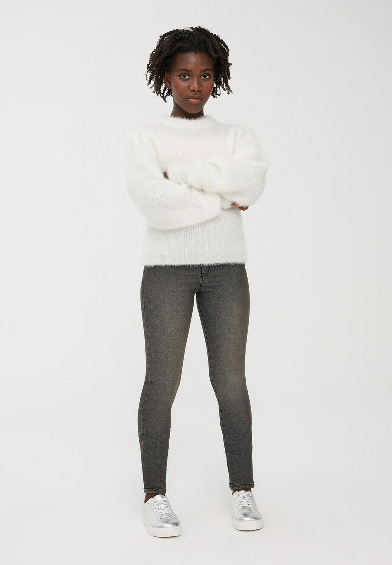 Biały, puszysty sweter z dzianiny z okrągłym dekoltem i bufkami, w połączeniu z ciemnoszarymi spodniami typu slim fit i srebrnymi sneakersami.