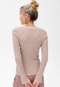 Beige geribbelde trui met lange mouwen en witte rand bij de halslijn en mouwen, met een aansluitend ontwerp en een zachte textuur.