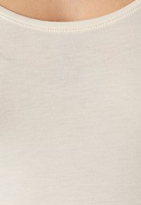 Tejido de rayas beige con una textura suave, que presenta un escote amplio y redondeado, y sutilezas en los detalles de costura a lo largo de los bordes.