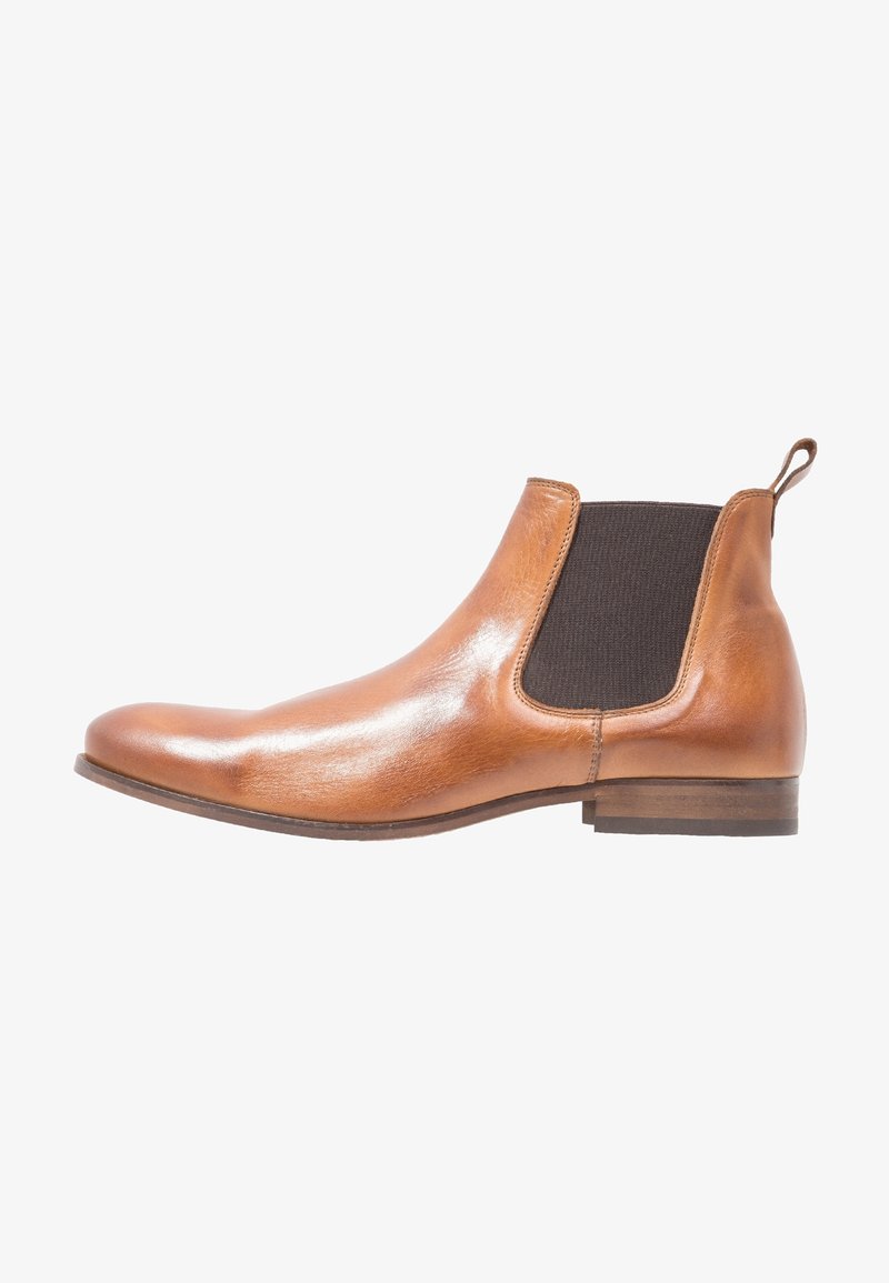 Bottine Chelsea en cuir fauve avec panneau latéral élastique sombre, petit talon et languette à l'arrière, montrée de profil sur fond blanc.