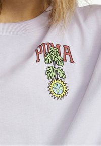 Hellvioletter Baumwollpullover mit rotem "PUMA"-Schriftzug und einer Grafik eines grünen Blattes und der Erde, umgeben von einer gelben Sonne.