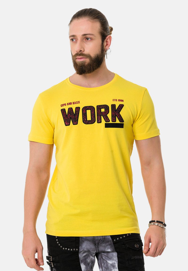 Gelbes Baumwoll-T-Shirt mit einem auffälligen schwarzen "WORK"-Graphic, Rundhalsausschnitt und kurzen Ärmeln. Sanfte Textur mit einer figurbetonten Passform.