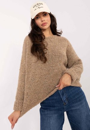 Beige knitted sweater with a textured, fuzzy appearance, featuring a wide neckline and long sleeves, paired with dark blue jeans and a cream hat.