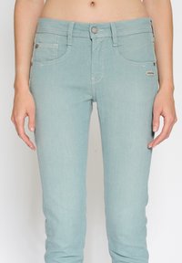 Jasnoniebieskie dżinsy z denimu o dopasowanym kroju, z pięcioma kieszeniami i kontrastującym, białym przeszyciem. Na boku widoczne jest małe logo.