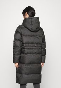 Abrigo acolchado negro con capucha, mangas largas y un diseño acolchado con secciones horizontales. Material suave con una textura lisa.