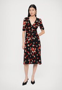 Vestido negro con corsé ajustado y falda acampanada, con un patrón de lunares multicolores en rojo y beige. Mangas cortas y escote en v.