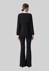 Top nero a maniche lunghe con scollatura rotonda e zip sul retro, caratterizzato da dettagli frangiati all'orlo. Abbinato a pantaloni neri a palazzo.
