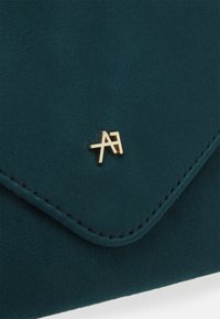 Turkusowa zamszowa kopertówka z złotymi dodatkami. Posiada design w kształcie koperty oraz obszyte krawędzie, z małym logo przy zapięciu.