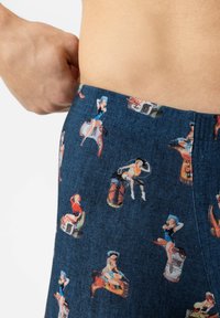 Plan rapproché d'une personne ajustant un short bleu foncé orné d'illustrations vintage de cowgirls pin-up dans diverses poses et tenues.