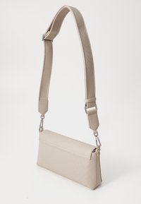 Sac à épaule beige en matériau texturé, de forme rectangulaire, avec une sangle amovible et des accents en métal argenté.