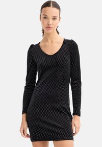 Vestido negro de manga larga con escote en V, decorado con lunares blancos, de forma ajustada y tejido texturizado. Hombros abullonados que aportan un detalle sutil.