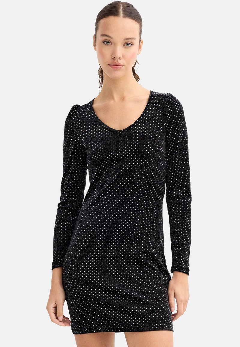 Vestido negro de manga larga con escote en V, decorado con lunares blancos, de forma ajustada y tejido texturizado. Hombros abullonados que aportan un detalle sutil.