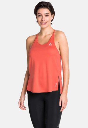 Woman wearing an orange sleeveless sports top and black leggings standing against a plain light background.