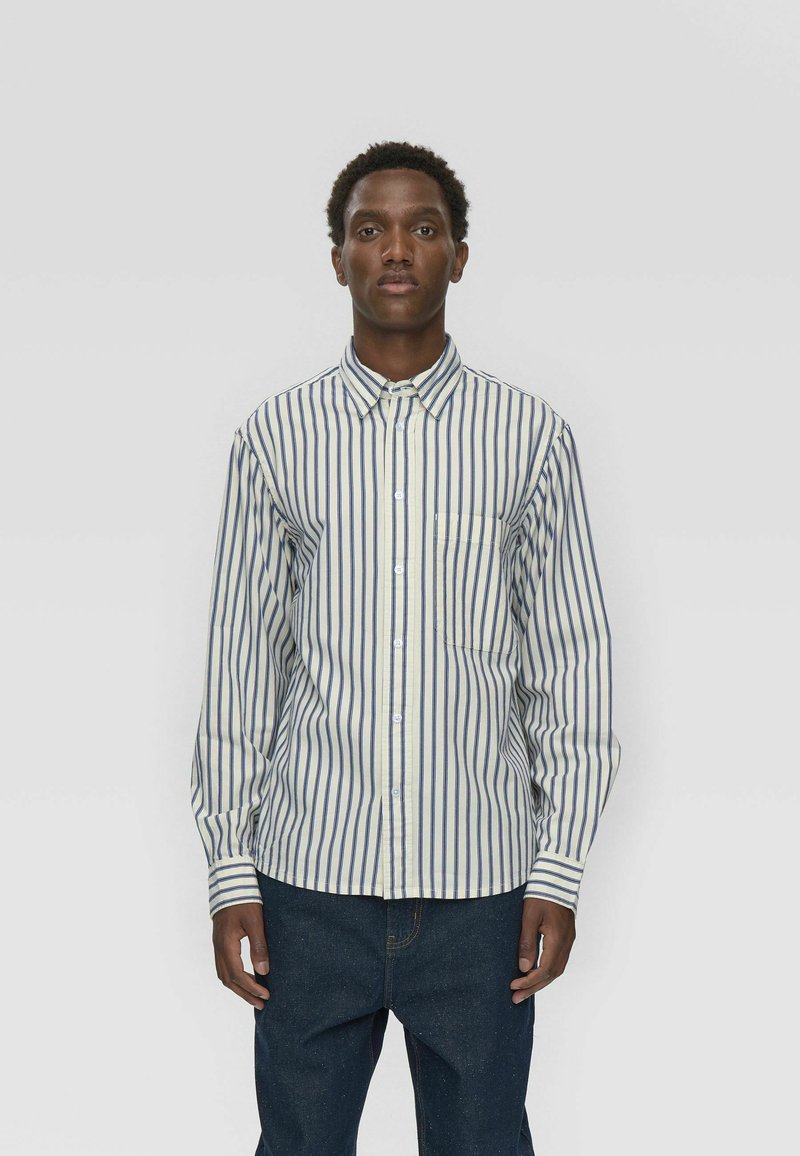 Chemise à rayures à manches longues en crème avec des rayures verticales navy et bleu foncé ; dotée d'un col boutonné et d'une poche. Tissu en coton.