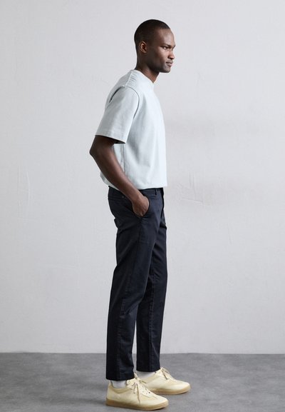 Sudadera de manga corta azul claro, pantalones ajustados negros y zapatillas crema con suelas de goma. Textura suave, diseño minimalista.