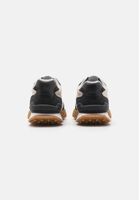 Lacoste tennised musta seemisnaha ja võrgupealsega, kreemikat tooniga aktsentide ning tekstuurse kummitallaga, millel on nähtavad mustrid.