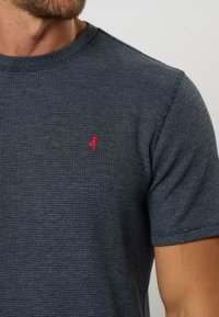 Camiseta de manga corta azul marino con una tela texturizada. Presenta un pequeño logo rojo en el pecho. Cuello redondo y corte relajado.