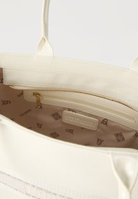 Εσωτερικό κρεμ τσάντας tote με χρυσή τσέπη φερμουάρ και μπεζ φόδρα τυπωμένη με λογότυπα "Steve Madden".