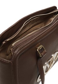 Bruine leren handtas met gouden ritscompartimenten en een gouden logo-accessoire aan de voorkant. Binnenkant gevoerd met beige stof.