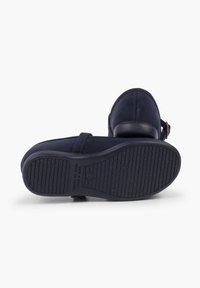 Zapatos de ante azul marino con punta redondeada, correa ajustable y suela de goma texturizada que presenta un patrón ondulado y un detalle de marca.
