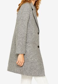 Abrigo de mezcla de lana gris con corte recto, grandes botones negros, cuello de solapa y bolsillos laterales. Presenta un acabado texturizado.