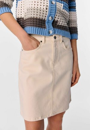 Beige denimrok met een rechte snit, voorzien van voorzakken en een zwarte knoopsluiting. De stof heeft een gladde textuur.