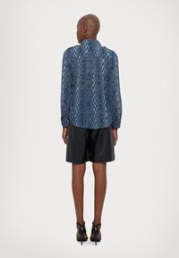Blå slangeskinnsmønster bluse med lange ermer og kragehals, kombinert med svarte skinnshorts og hælsandaler.