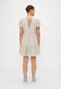 Σαρκώδη μπεζ φόρεμα με φουσκωτά μανίκια, V-ανοιχτή πλάτη και tiered φούστα. Κατασκευασμένο από υφασμένο ύφασμα, διαθέτει δεσμευτική κλείσιμο και διακοσμητικά αξεσουάρ.