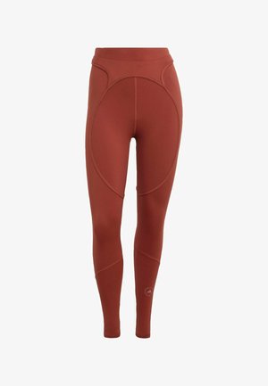 Leggings de cintura alta y largo completo de color óxido con detalles de costuras curvas y un logo de la marca cerca de la parte inferior de la pantorrilla sobre un fondo blanco.
