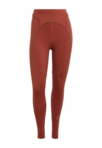 Leggings in Rostfarbe mit hoher Taille und voller Länge, geschwungene Nahtdetails und ein Markenlogo nahe der unteren Wade auf weißem Hintergrund.